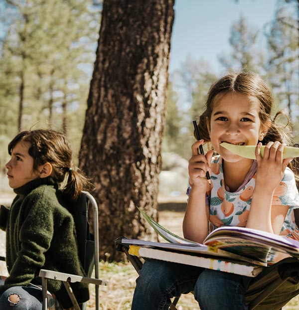 Two children enjoying a sunny outdoor setting, one eating a snack and the other lost in thought.