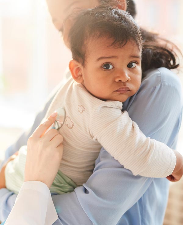 A caregiver holds a baby while checking the child's heartbeat with a stethoscope, showcasing a nurturing health check-up setting.