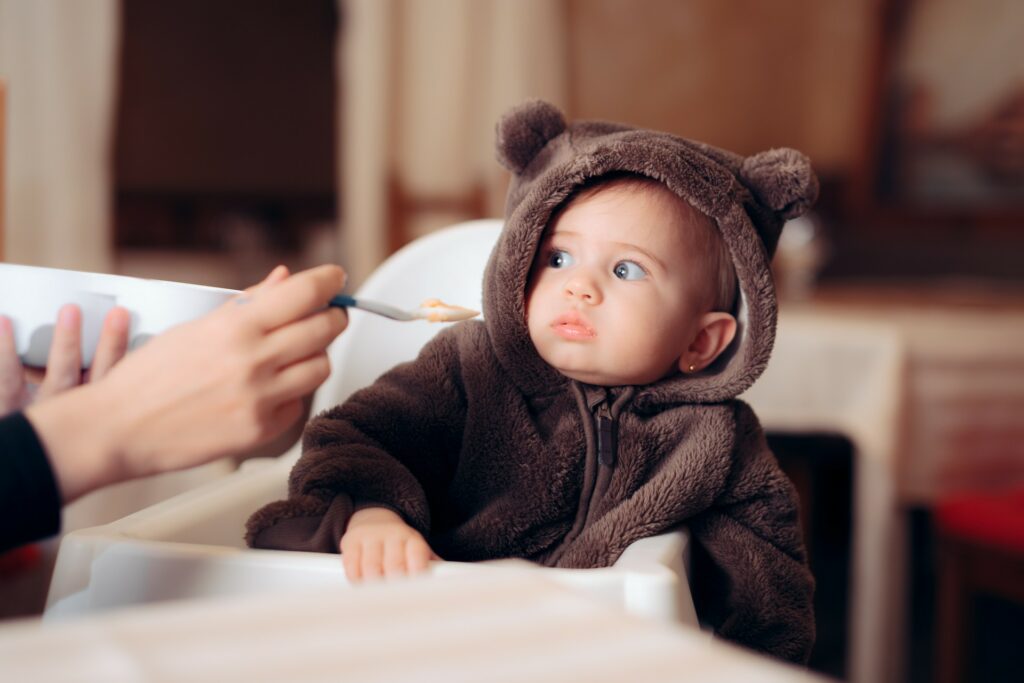 Picky eater avoids eating food on a spoon held by a parent.