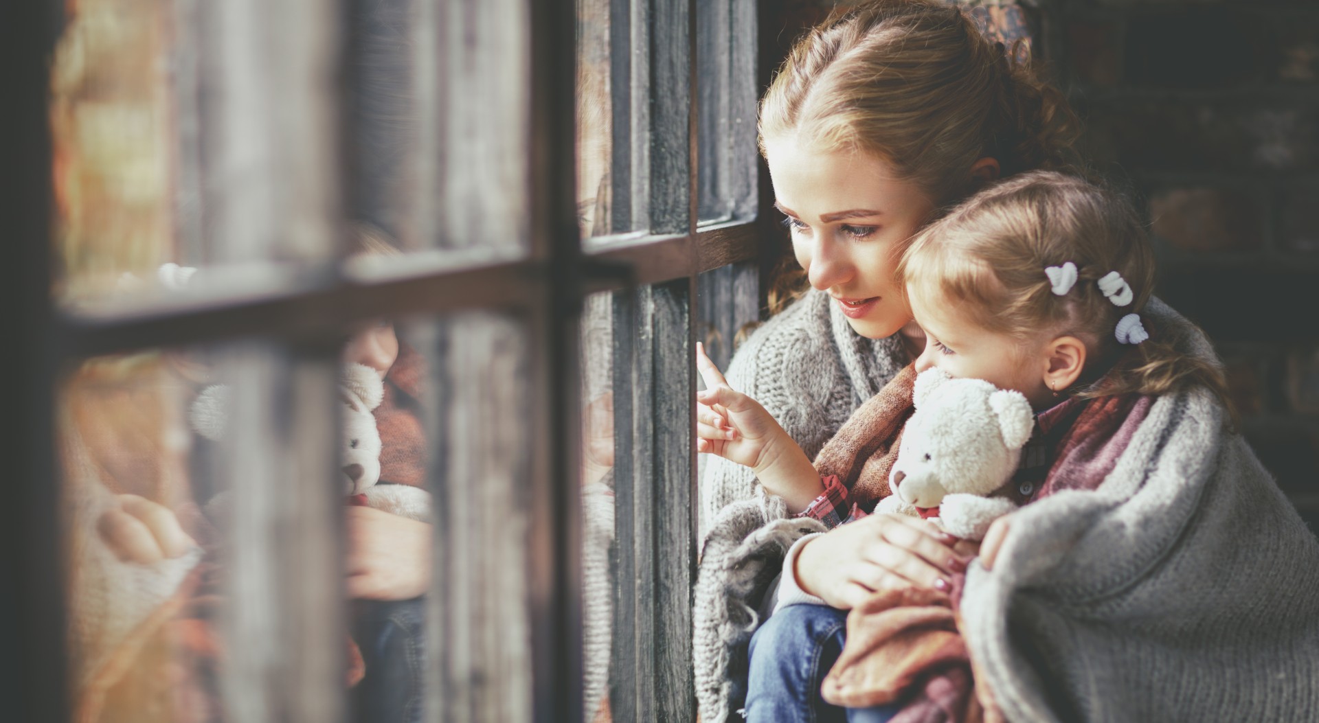 Mother holds sick child in her arms as they look out the window together.