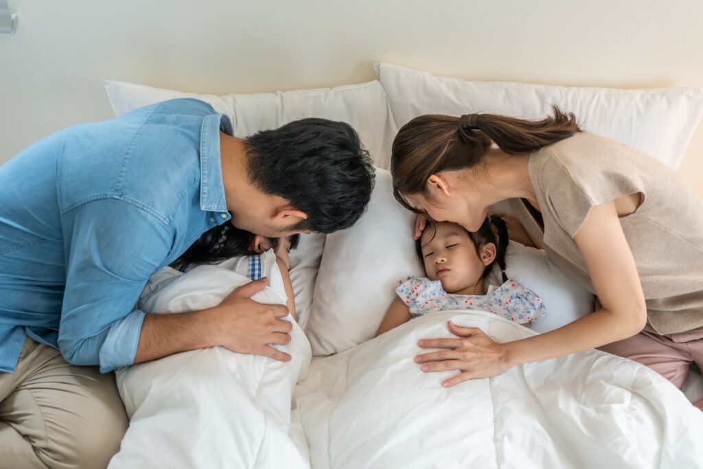 Two parents kiss their two children goodnight.