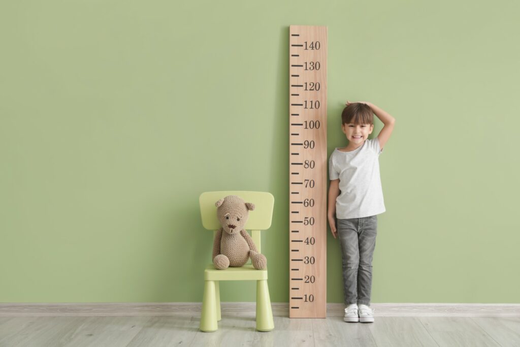 Child stands next to a large ruler to indicate height measurement in growth charts.