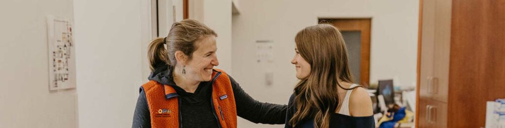 Two women smiling and engaging in conversation in a warm indoor setting.