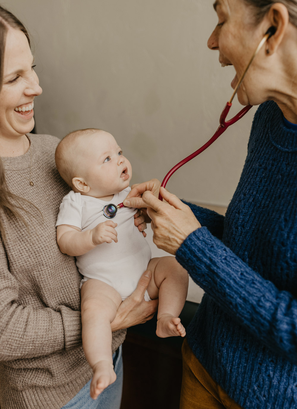 A woman and a healthcare professional smile at a baby during a check-up, creating a joyful and caring atmosphere.
