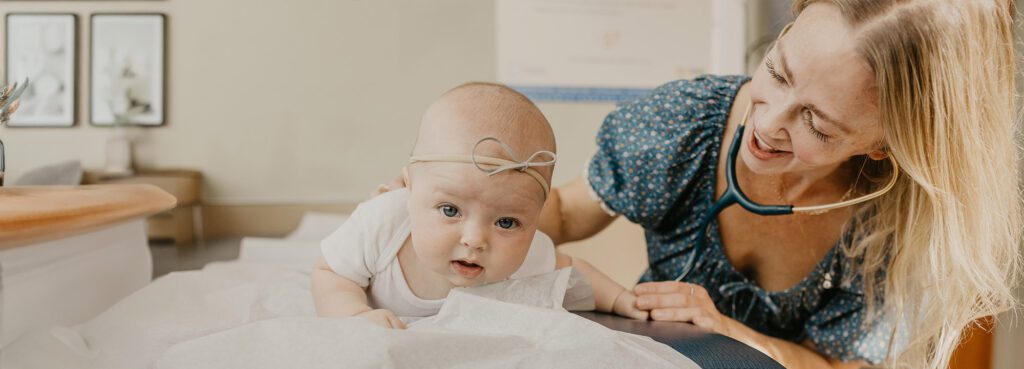 A baby lies on a table with a caring adult nearby, both engaged in a joyful interaction.