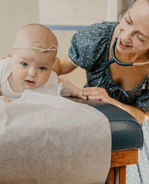 A baby with a headband explores a surface while a smiling adult interacts closely, creating a warm, caring atmosphere.
