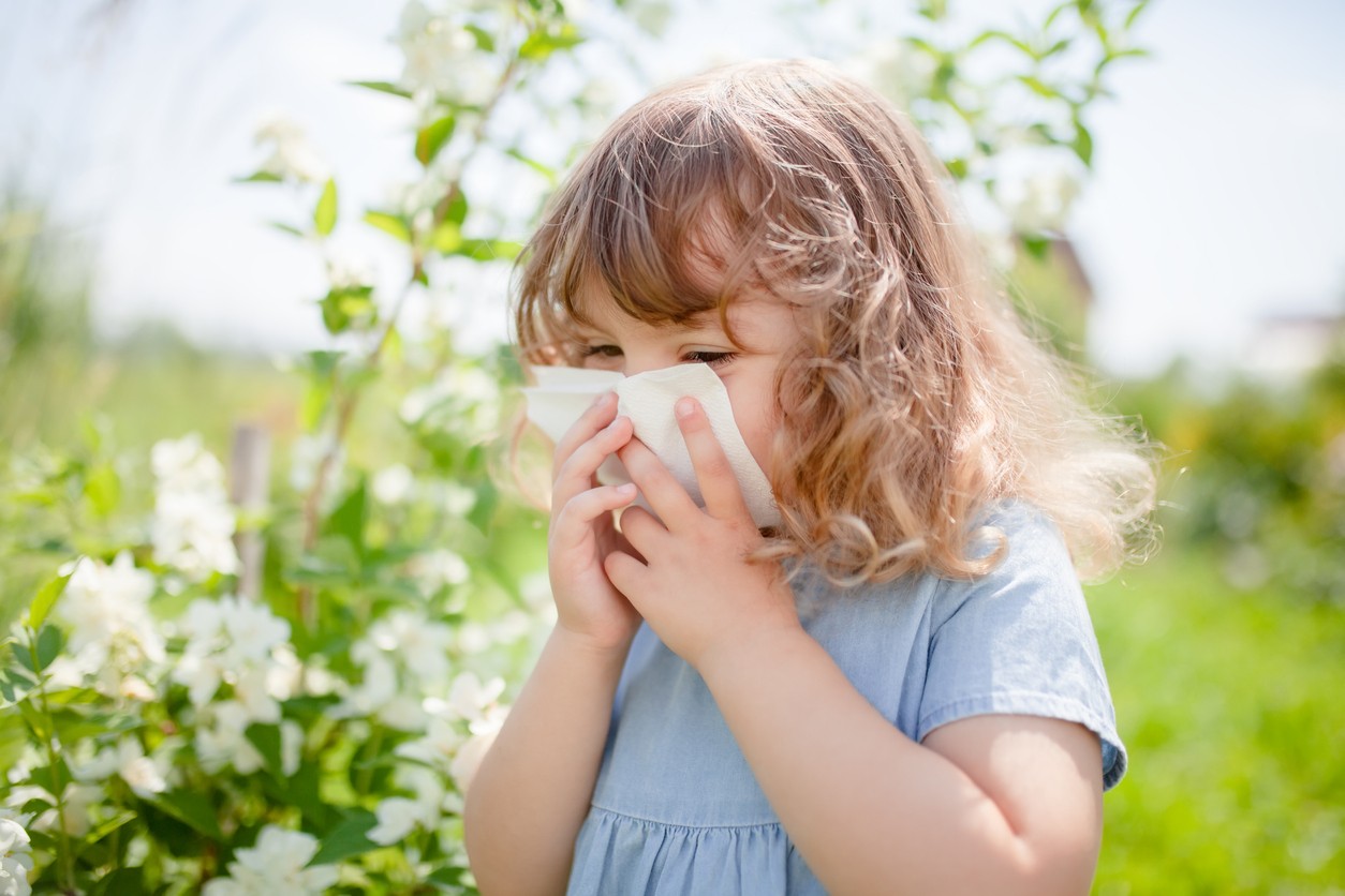 Girl blowing into a tissue while outside on a field.