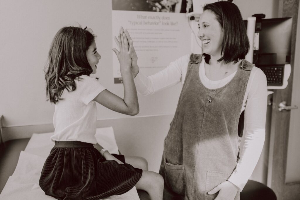 A pediatrician high-fiving a young patient after a check up.